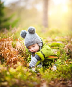 Un bébé joue avec de la mousse et des fougères dans un bois naturel sous un rayon de soleil en automne